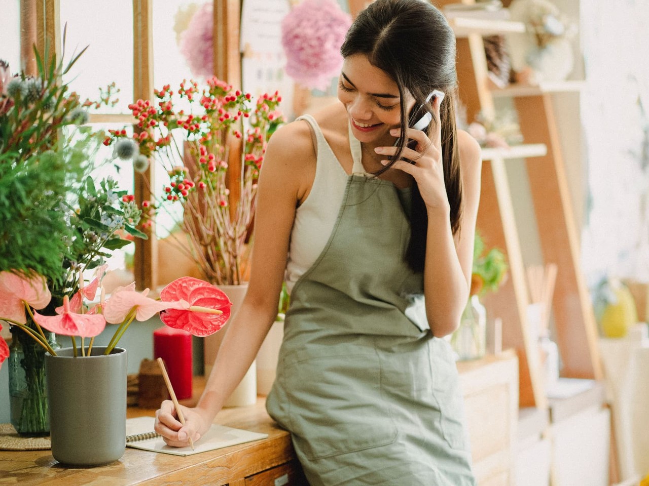 Florist and small shop owner taking a customer order by phone among flowers and plants